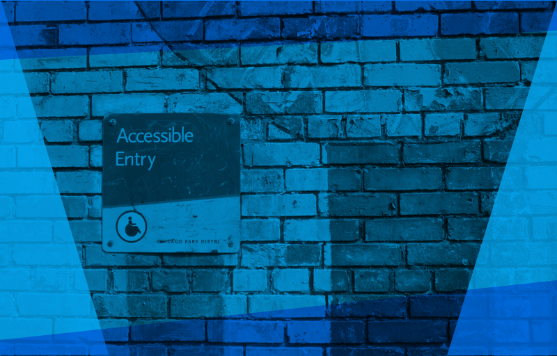 Accessible entry sign on a graffiti-covered brick wall.